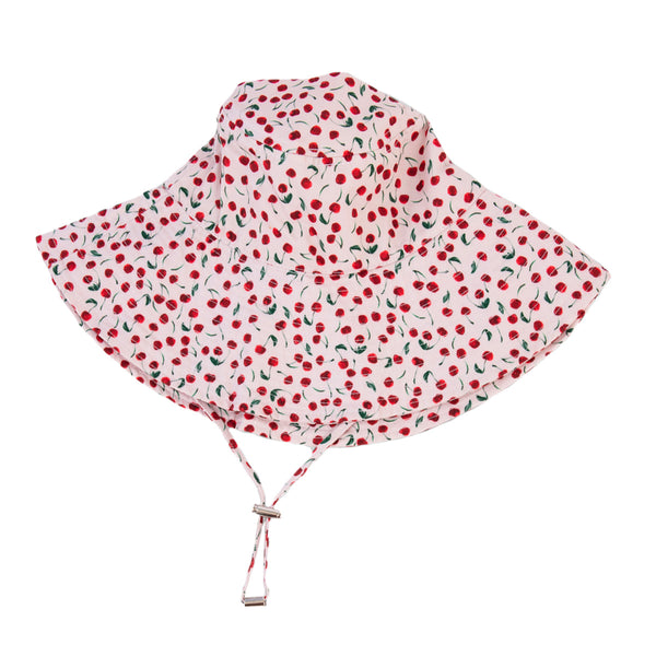 A white cream hat featuring a red cherry print with green leaves, set against a plain white background. 