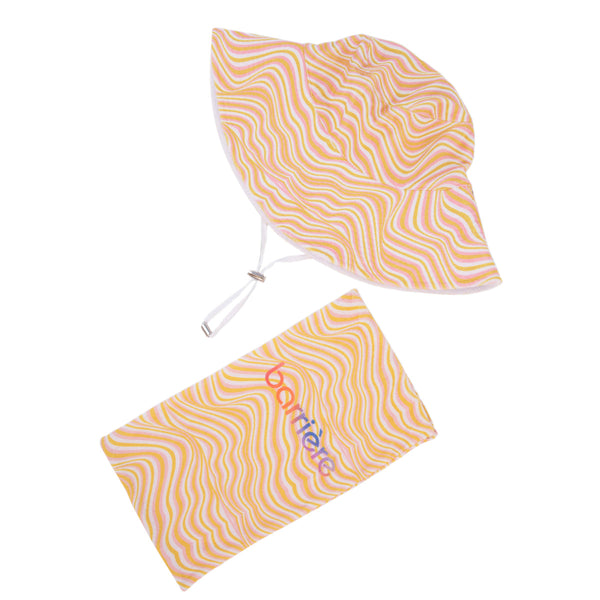 A reversible sun hat with a multi-colored pattern, featuring wavy lines in shades of orange, yellow, and white. Next to the hat is a bag with “Barriere” written on it.